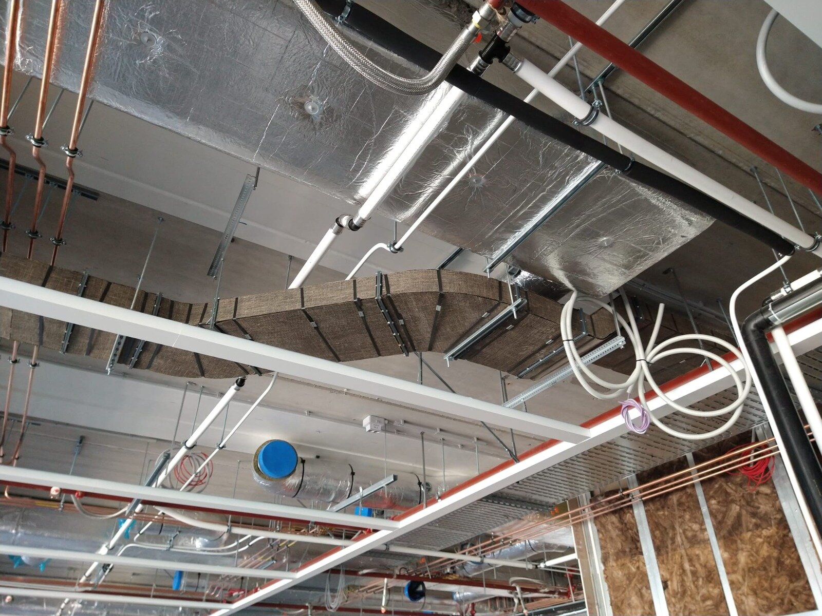 Luchtkanalen geïsoleerd met steenwol en aluminiumfolie tussen leidingen onder een plafond