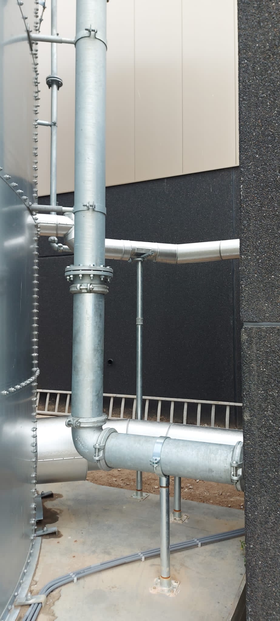 Gegalvaniseerde leidingen met flensverbinding en aluminium ommantelde leidingen naast een opslagtank