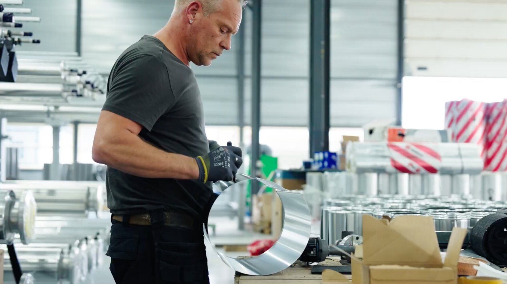 Medewerker buigt een aluminium mantel rond in de werkplaats tussen voorraad leidingdelen