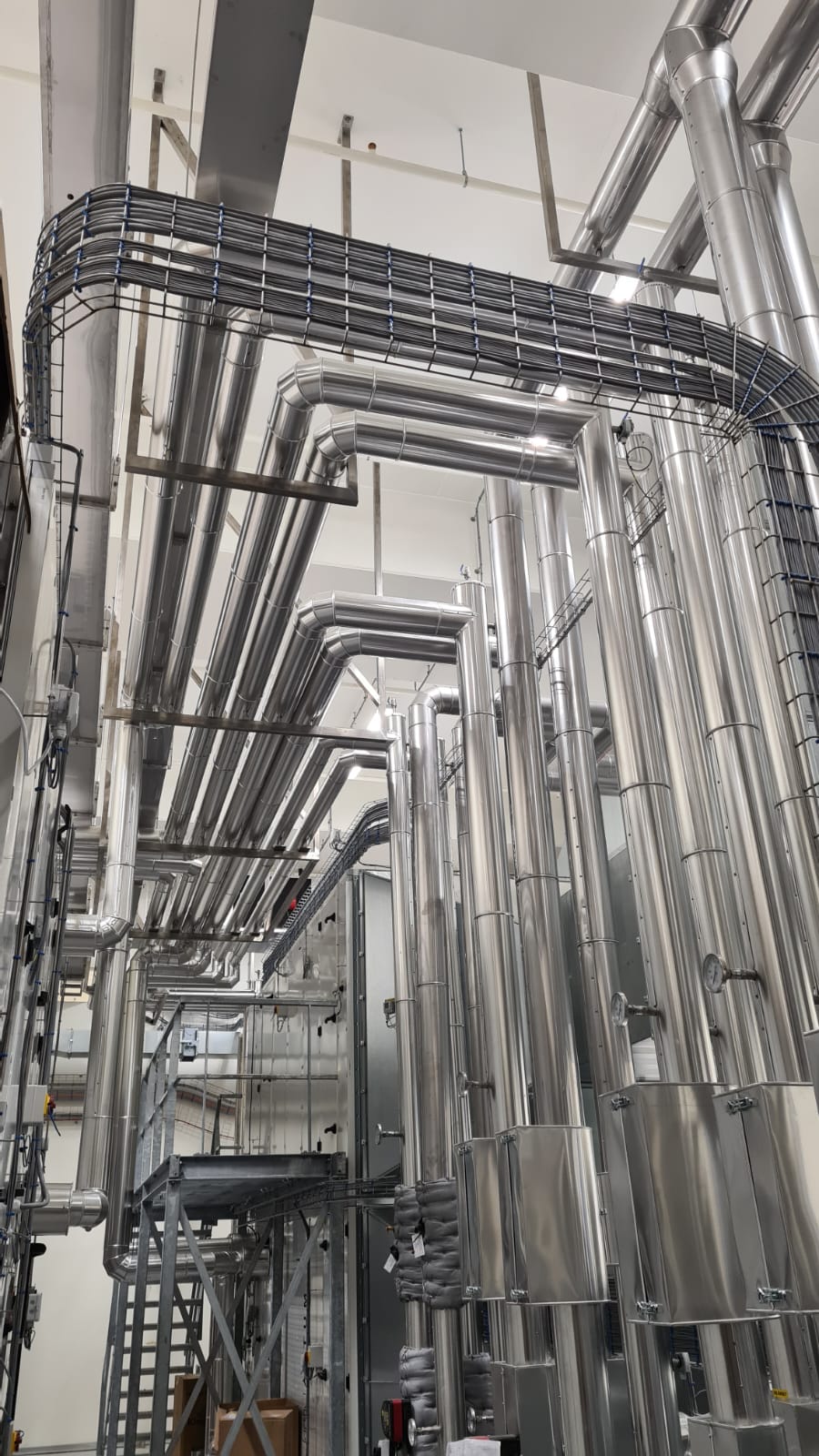 Hoge leidingbundels met aluminium ommanteling langs kabelgoten in een technische ruimte