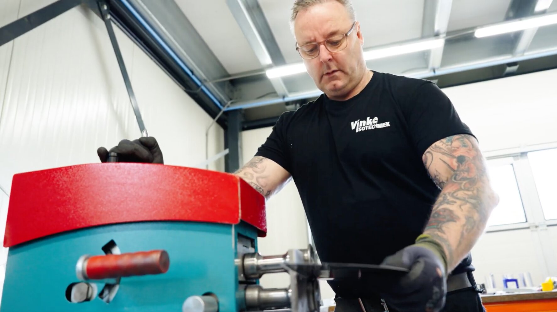 Medewerker van Vinke Isotechniek voert een plaatstrook door een rolmachine in de werkplaats