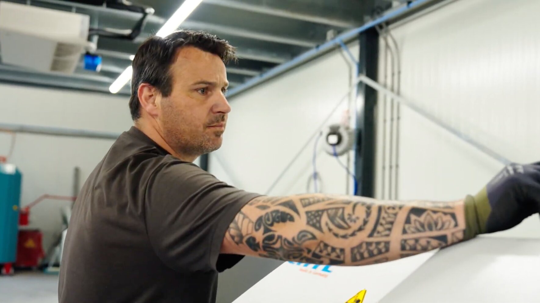Medewerker met getatoeëerde arm aan het werk bij een witte machine in de werkplaats
